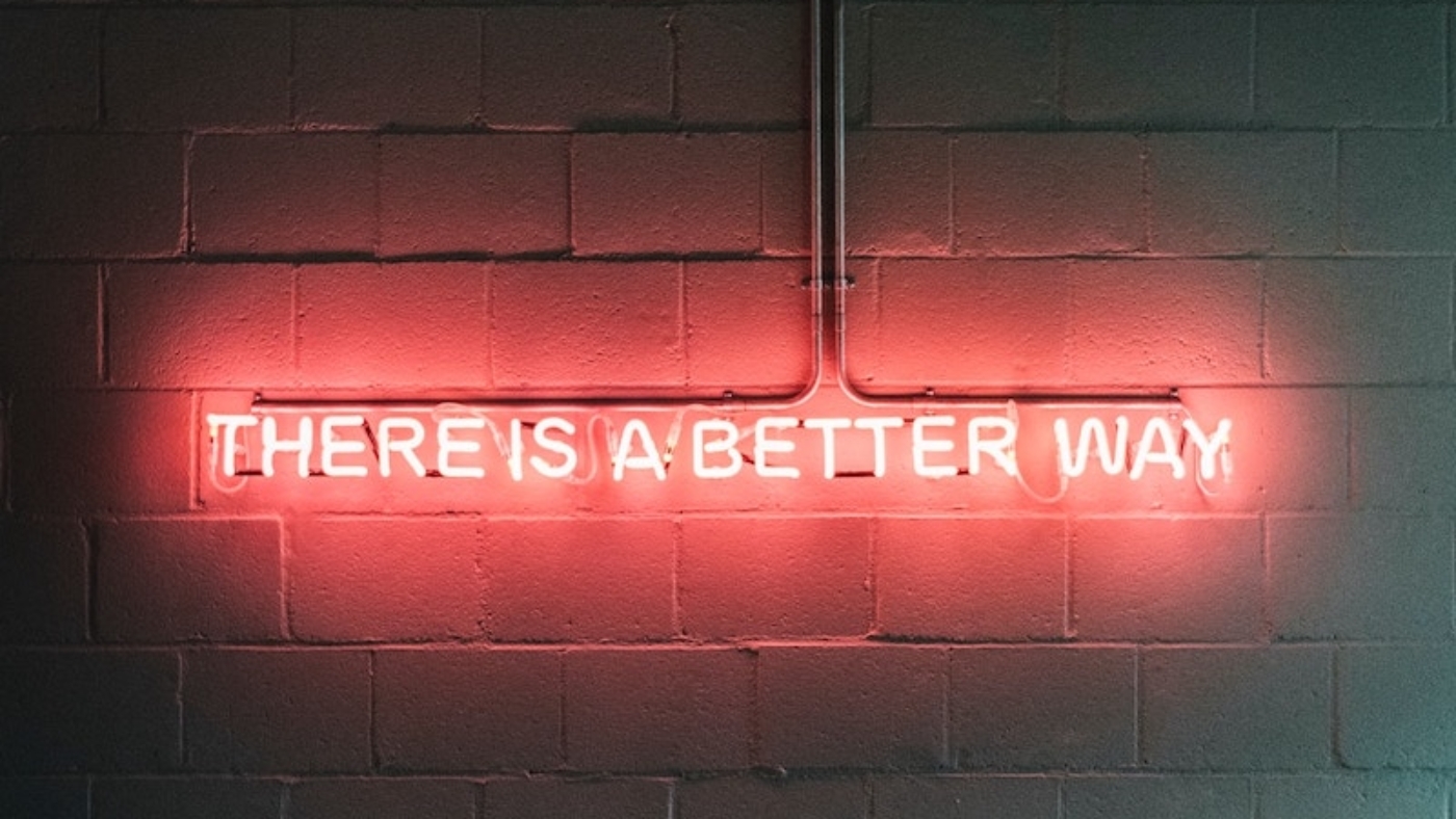 A red neaon sign against a brick wall. It reads: there is a better way.